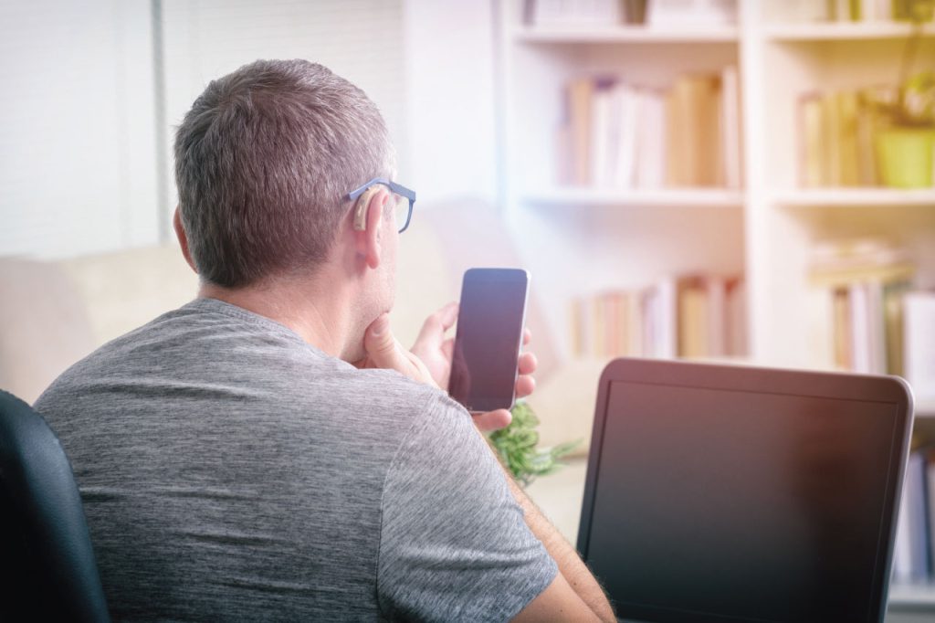 A man with hearing impairment working on a laptop and looking at a mobile phone