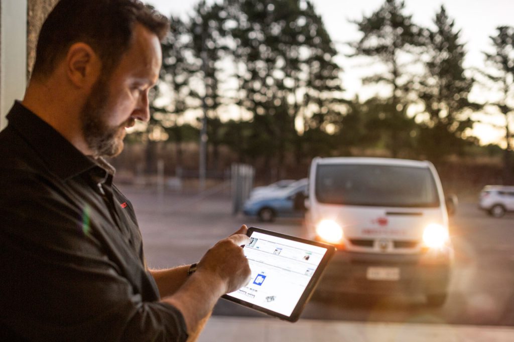 A Telstra technician using a tablet device with a service van in the background