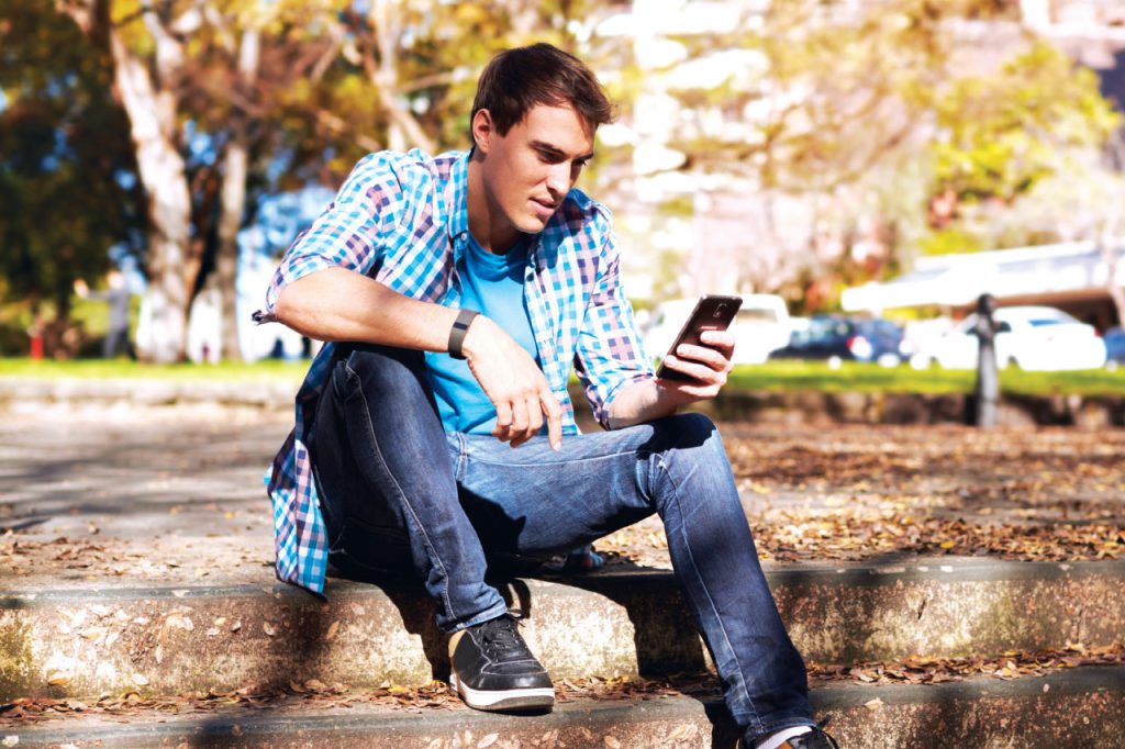 a young male using a mobile phone sitting outside on stairs