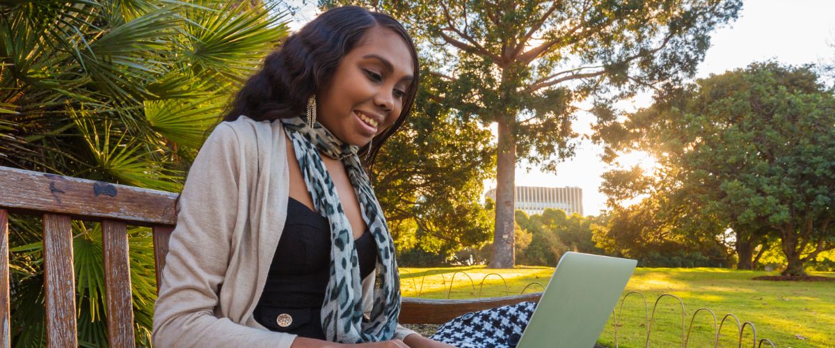 First Nations woman using a laptop in the park on a sunny day