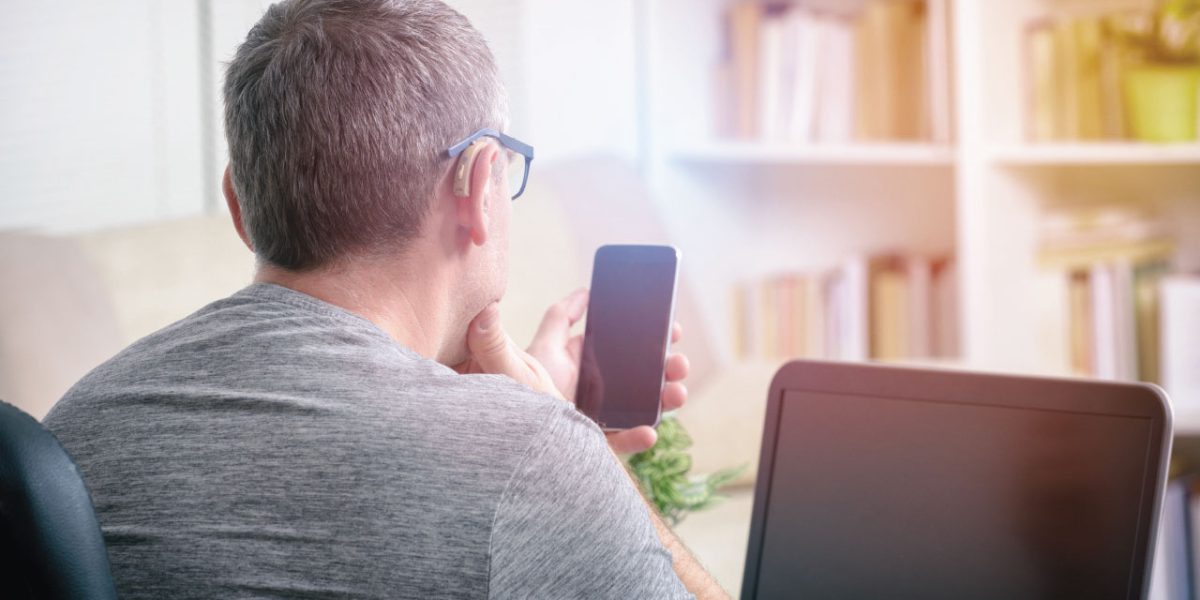 A man with hearing impairment working on a laptop and looking at a mobile phone