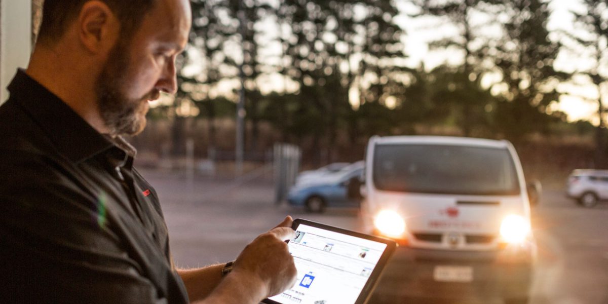 A Telstra technician using a tablet device with a service van in the background