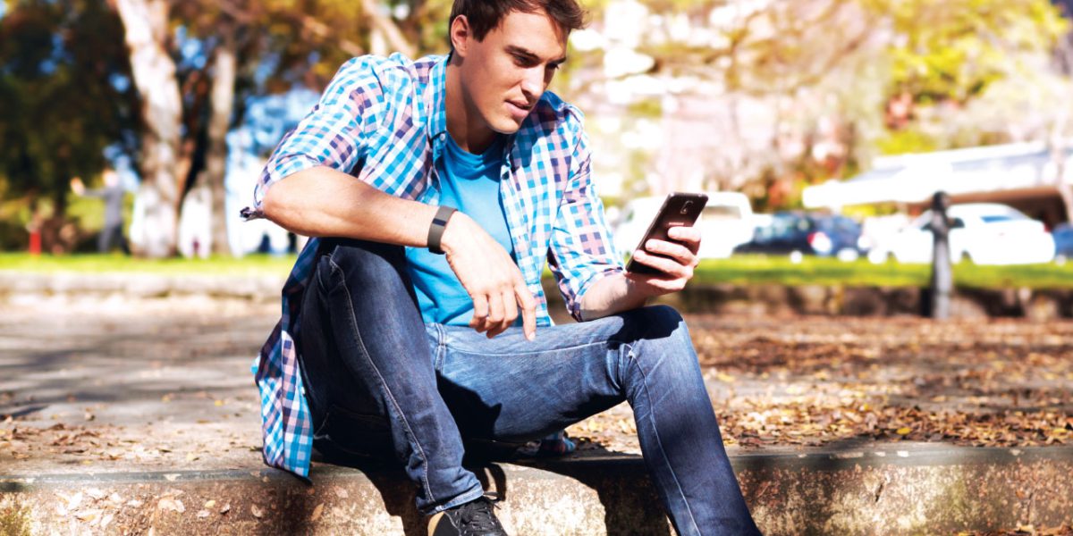 a young male using a mobile phone sitting outside on stairs